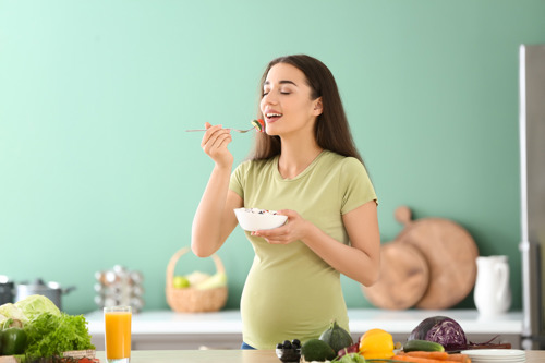 Pregnant woman eating healthy food consisiting of nuts, yoghurt, avocado and cereals.
